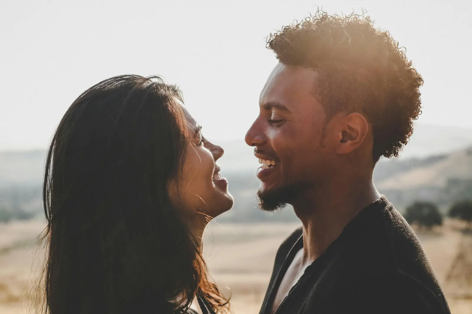A couple laughing face to face outdoors in warm evening light