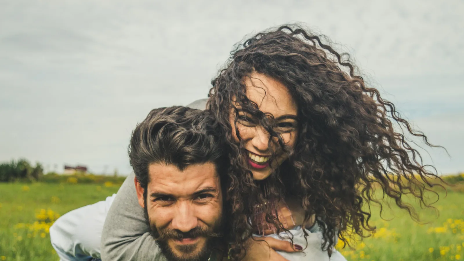 A couple laughing in a green meadow, the woman riding piggyback on the man