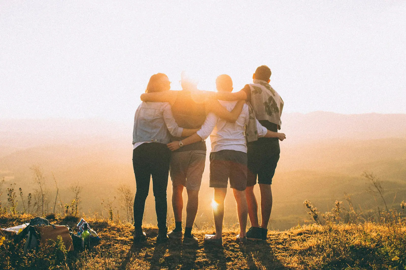 Four friends with their arms round each other, watching the sun set over the hills